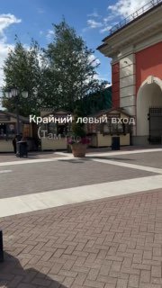 Кадр из короткого видеомаршрута: площадь у фасада Outlet Village Пулково, подпись «Крайний левый вход», пешеходная зона и ориентиры.