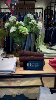 Витрина DIGEL в Outlet Village Pulkovo: стол с аккуратно сложенными вещами, табличка DIGEL и костюмы на вешалках на заднем плане.