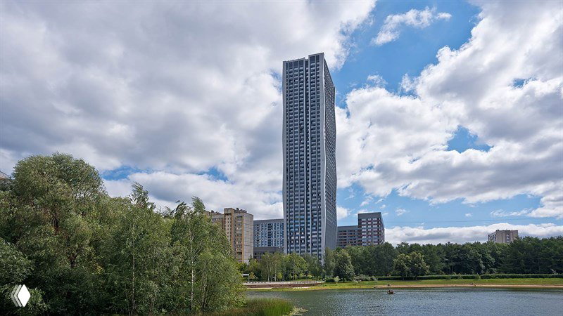 Небоскрёб на фоне облачного неба и озера: фактурный фасад, высотная доминанта в зелёной локации северо‑востока Москвы, вид с парка.