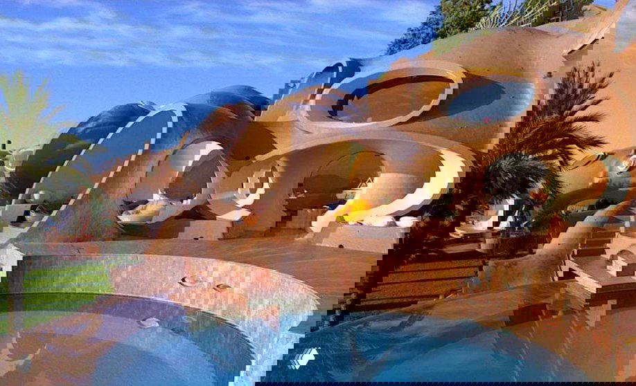 Дневной фасад пузырчатой виллы с круглыми жилыми капсулами, террасой и небольшим бассейном у моря