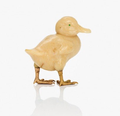 Изображение маленькой антикварной фигурки утёнка кремового оттенка с позолоченными лапками и заметным зелёным камушком в качестве глаза