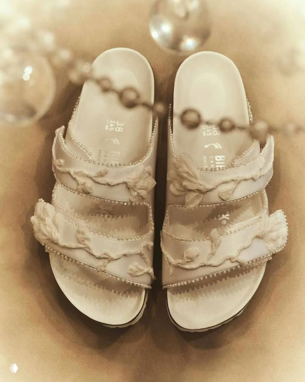 Крупный план белых сандалий Birkenstock из коллаборации Danielle Frankel с тканевыми декоративными элементами и жемчужными акцентами сверху