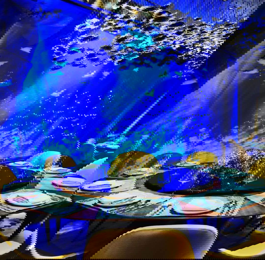 Интерьер рыбного ресторана отеля с большим обзорным аквариумом, круглым сервированным столом и синим подводным освещением на заднем плане.