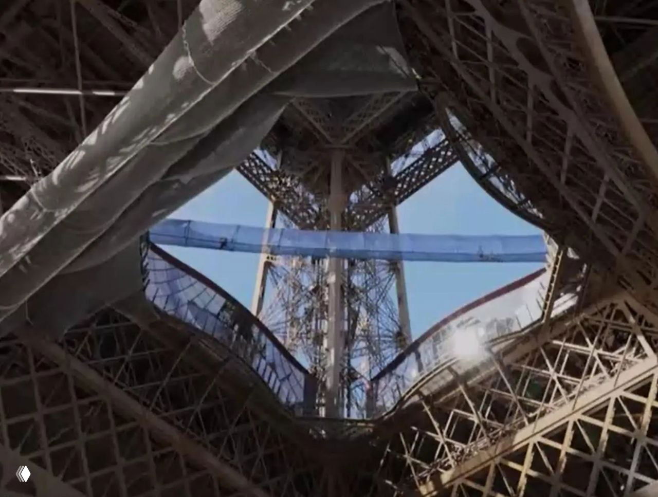 Вид снизу на середину Эйфелевой башни с натянутым синим мостом между опорами; заметна ажурная ферменная конструкция металла.