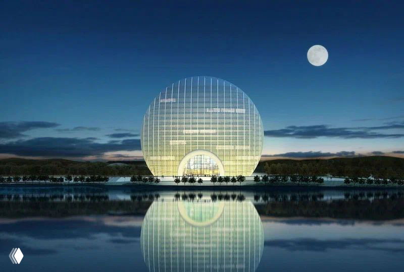 Построение Sunrise Kempinski вечером, фасад подсвечен жёлтым светом и отражается в воде, на небе видна луна.