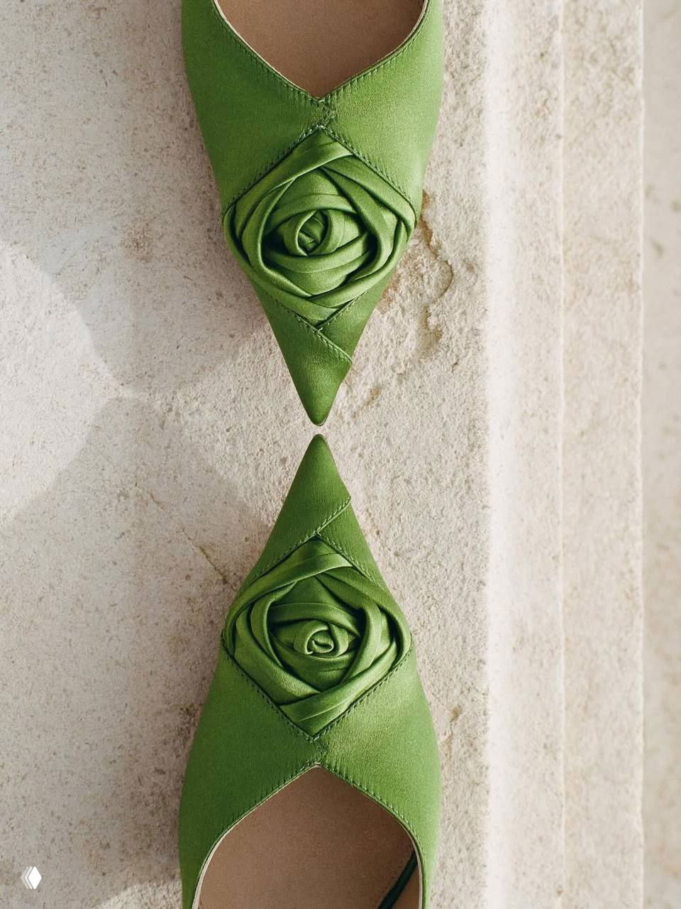 Пара заострённых зелёных туфель с декором «роза» на носке, выложенные симметрично на светлой колонне — деталь коллекции Dior.