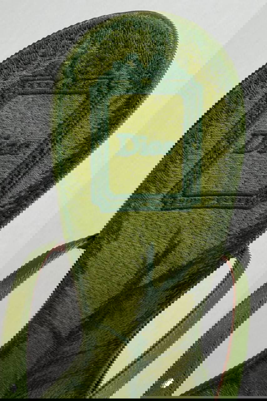 Подошва зелёной обуви с вышитым логотипом Dior и фактурной бархатной поверхностью — деталь производства и брендинга.