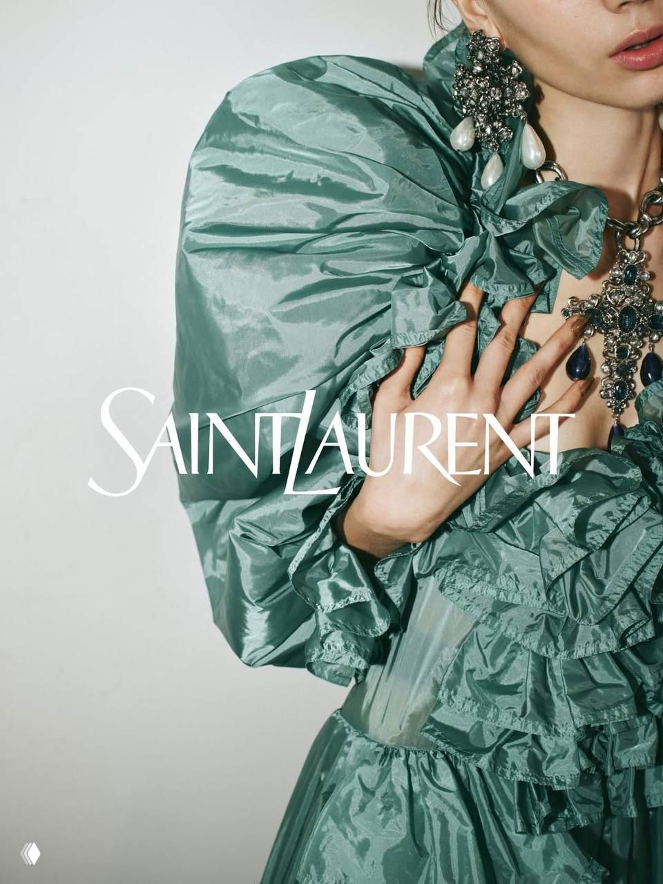 Крупный план мятно‑бирюзового платья Saint Laurent с воланами и массивными украшениями на шее, акцент на материале и декоративных деталях.