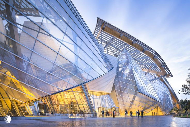 Вечерний вид криволинейных стеклянных и титановых фасадов резиденции Louis Vuitton: игра света на металлических поверхностях и люди у входа.