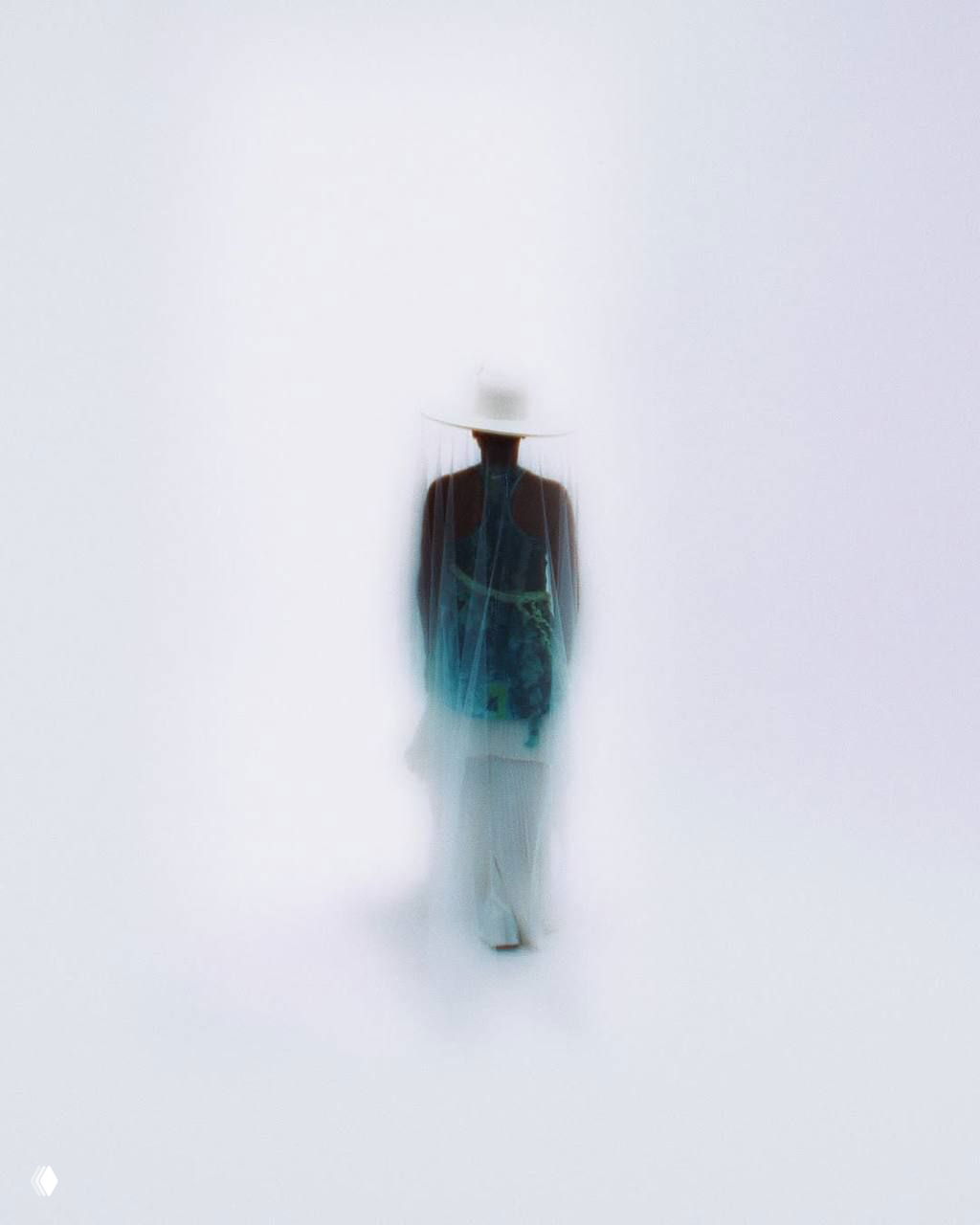 Размытый кадр модели, удаляющейся в глубину светлой студии, акцент на шляпе с вуалью и воздушную атмосферу показа/лука.