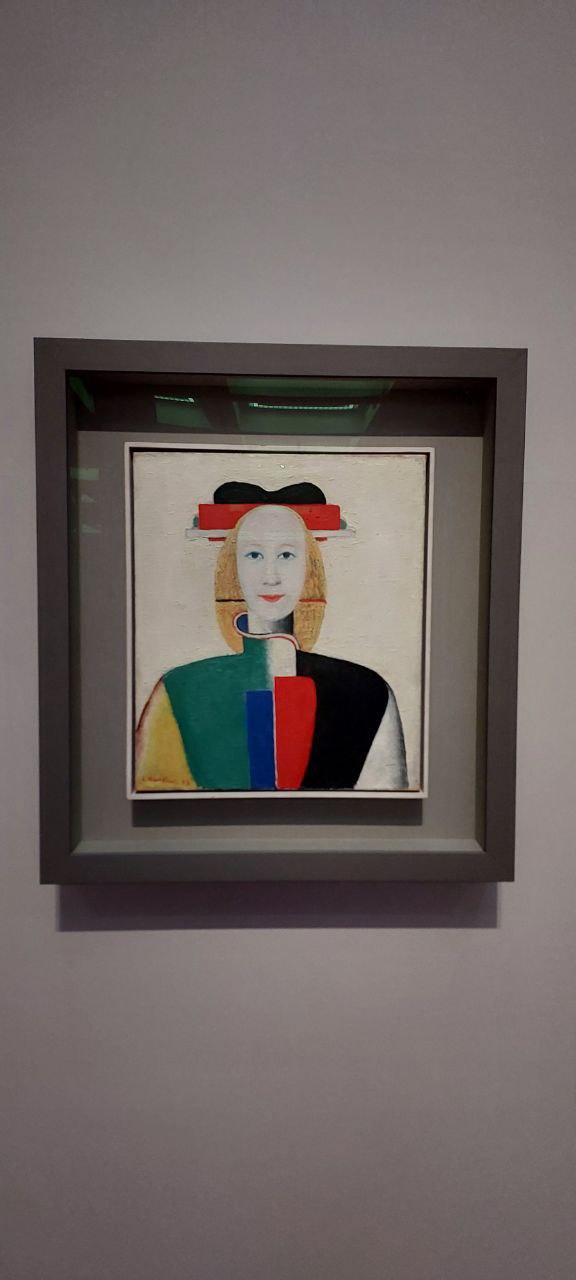Фотография портрета в рамке в авангардном стиле: условное лицо и цветовые блоки на светлом фоне, экспонируемого в музее.