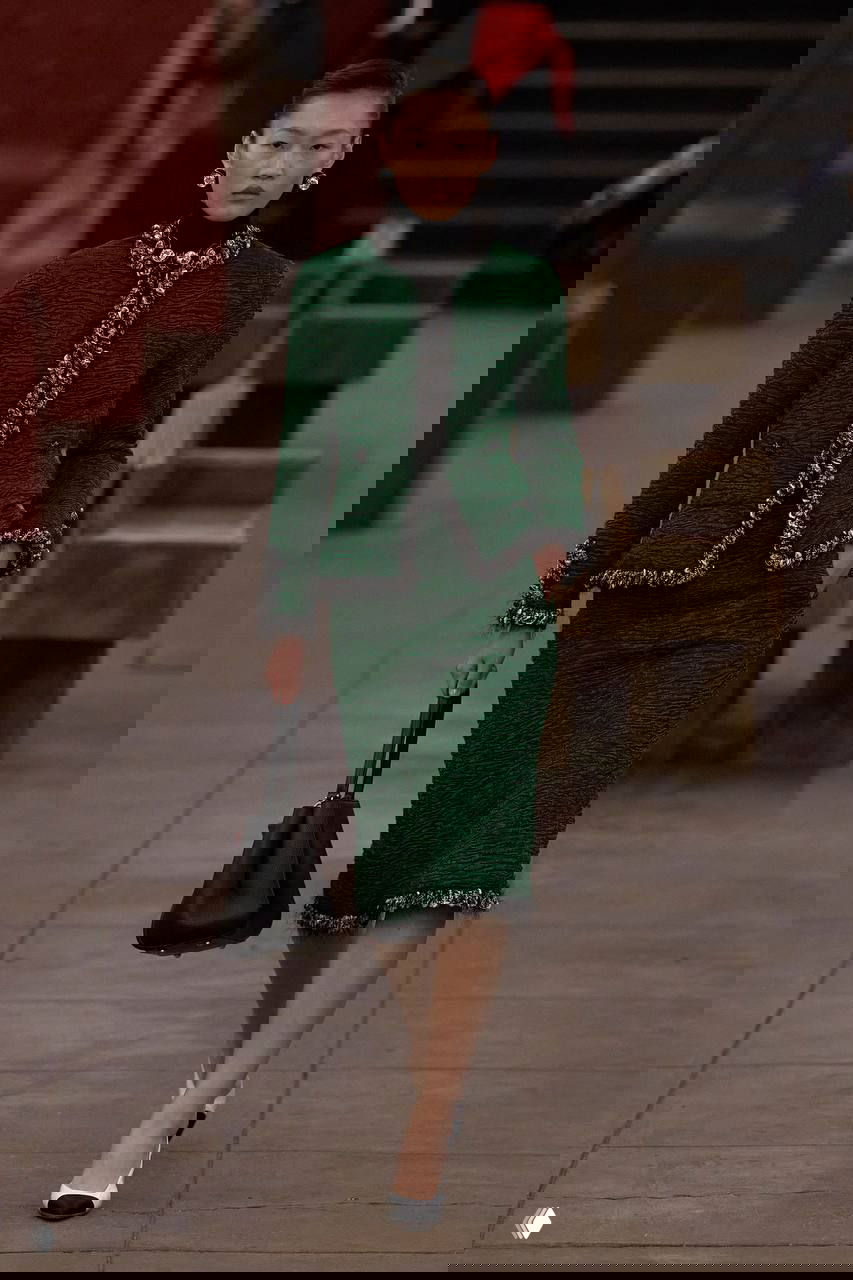 Модель в зеленом твидовом костюме и жемчужных серьгах дефилирует по перрону станции метро в рамках показа Métiers d’art дома Chanel в Нью‑Йорке.