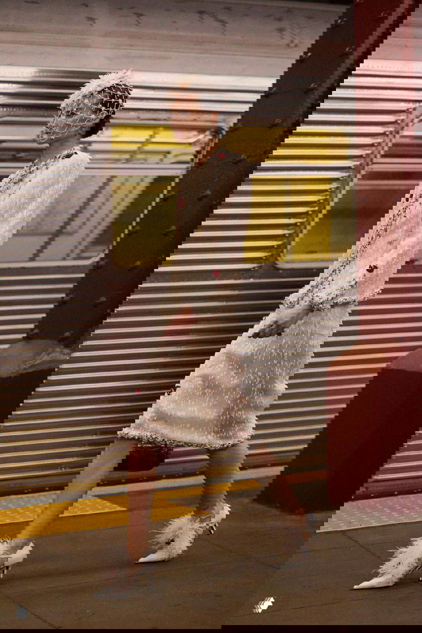 Модель в светлом твиде и декоративной вуали на голове проходит мимо вагона метро в ретро‑стиле во время показа Métiers d’art дома Chanel в Нью‑Йорке.