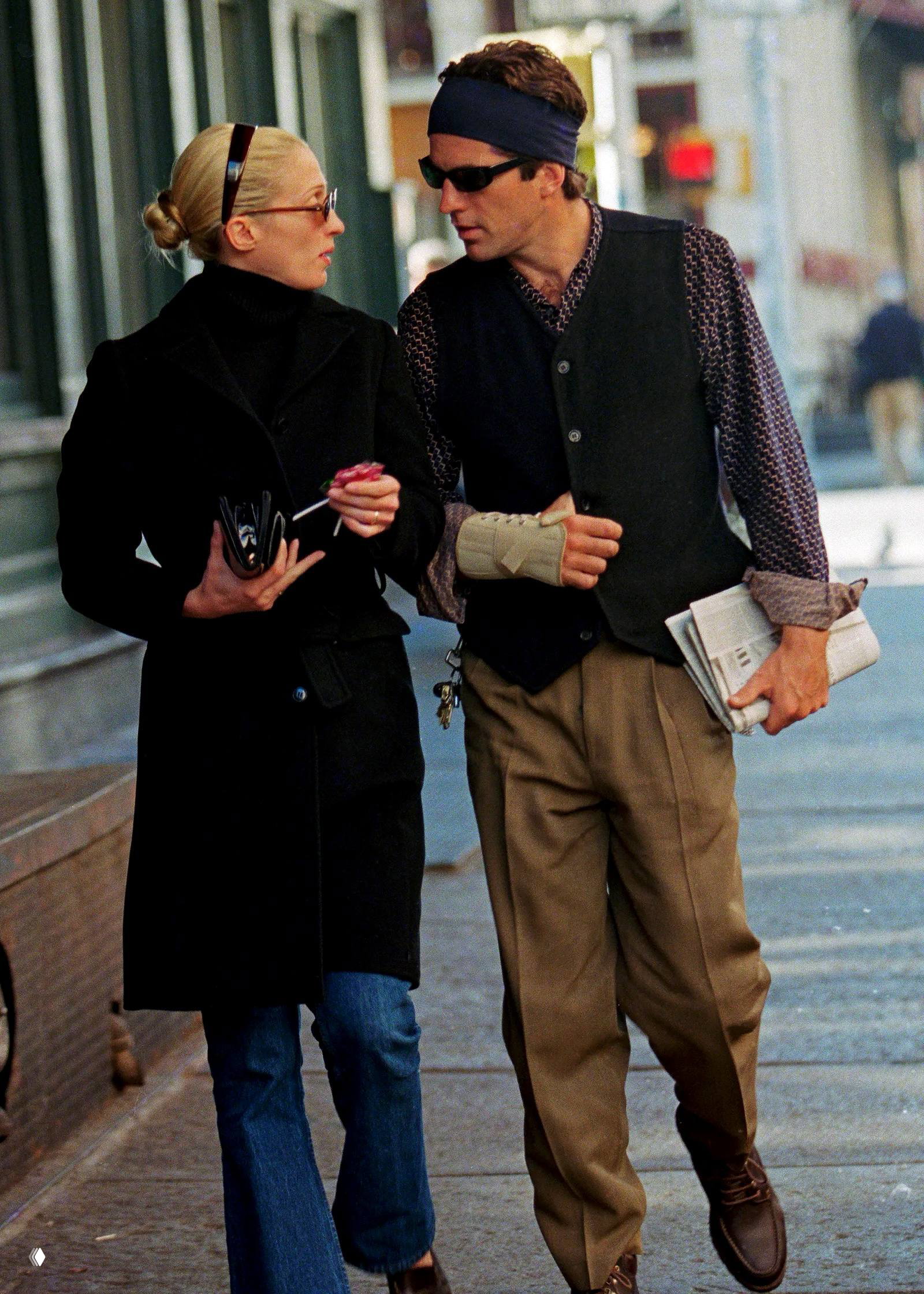 Мужчина и женщина идут по улице; мужчина в жилете и повязке на голове держит в руках газету — уличная сцена с повседневной эстетикой.