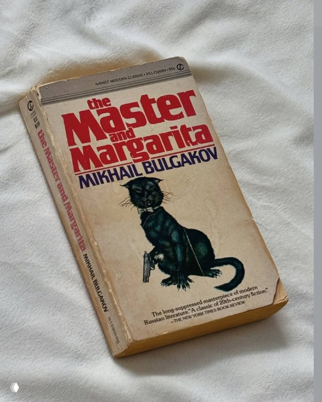 Старое издание «Мастер и Маргарита» Булгакова на белой ткани; пожелтевший переплёт и шрифты создают ощущение близости к классике и личной библиотеки.
