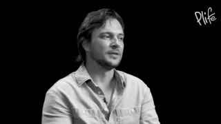 Чёрно-белый портрет мужчины в полуобороте, говорящего в интервью; логотип Plife в правом углу, задумчивая атмосфера.