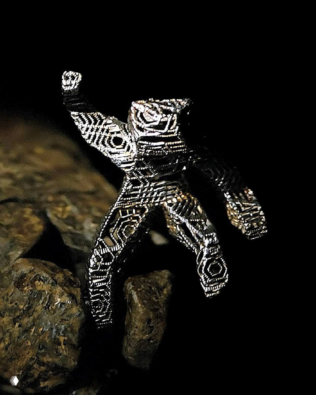 Макро-снимок небольшой металлической фигурки или талисмана на фоне камней и реквизита — деталь, добавляющая текстуру мира фильма.