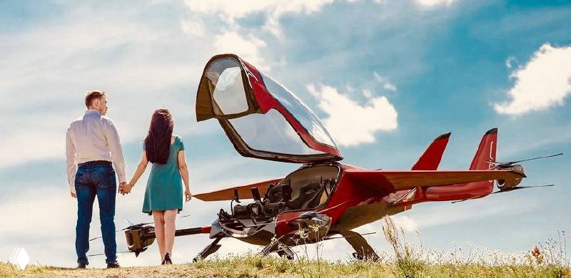 Красный двухместный прототип eVTOL Air One на земле с открытой кабинкой; рядом стоят двое, подчёркивая идею персонального владения и компактности.