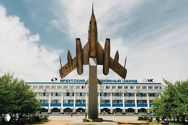 Монумент в виде самолёта на постаменте на фоне главного корпуса Иркутского авиационного завода ОАК — фасад завода и небо.