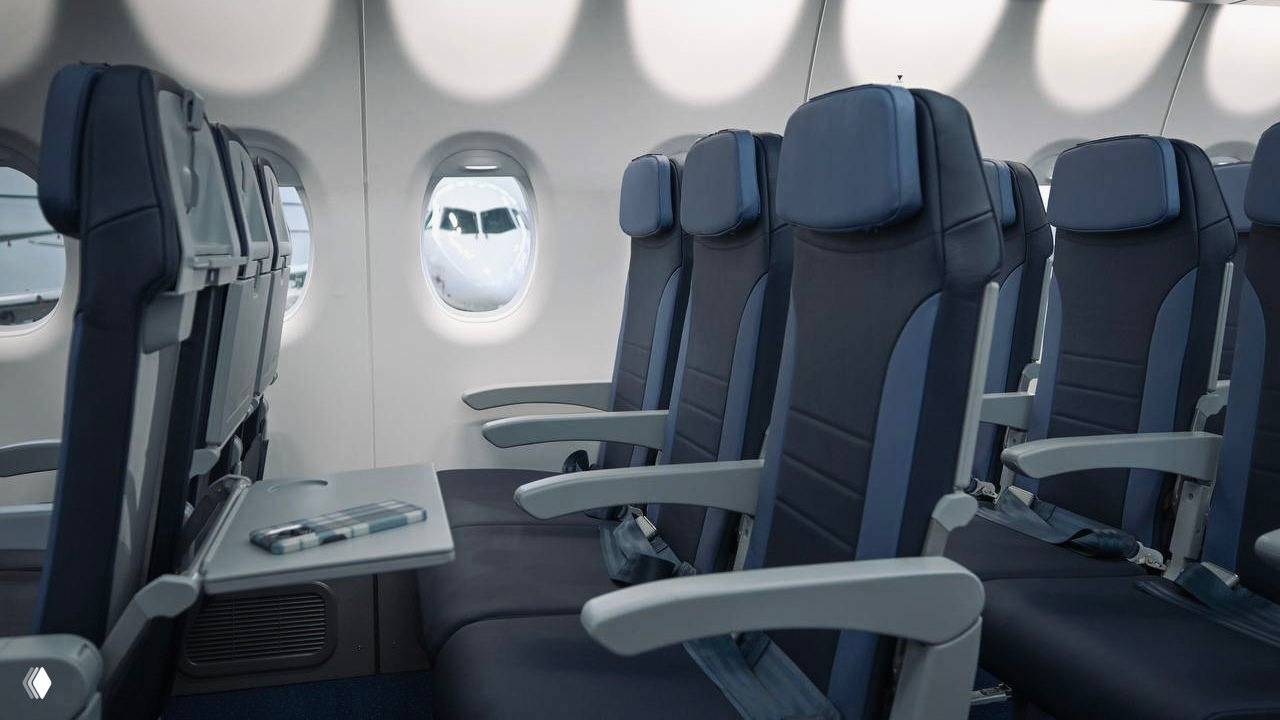 Интерьер пассажирского салона самолёта с рядами кресел, иллюминаторами и планшетом на откидном столике, компоновка на 100 пассажиров.