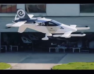 Прототип EHang VT35 на испытательном поле у ангара: небольшой двухместный автономный eVTOL с видимыми роторами и шасси при тестовом взлёте.