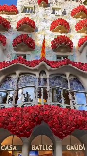 Фасад дома Бальо (Casa Batlló) в Барселоне, украшенный мозаикой, стеклянными осколками и яркими цветами; видна волнистая крыша и декоративные балконы в стиле Гауди.