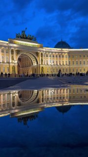 Вечерний вид арки Главного штаба на Дворцовой площади в Санкт-Петербурге с архитектурной подсветкой и зеркальным отражением в лужах.