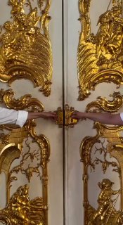 Крупный план позолоченных декоративных дверей дворца Шарлоттенбург в Берлине: барельефы, резные элементы и позолоченные ручки.