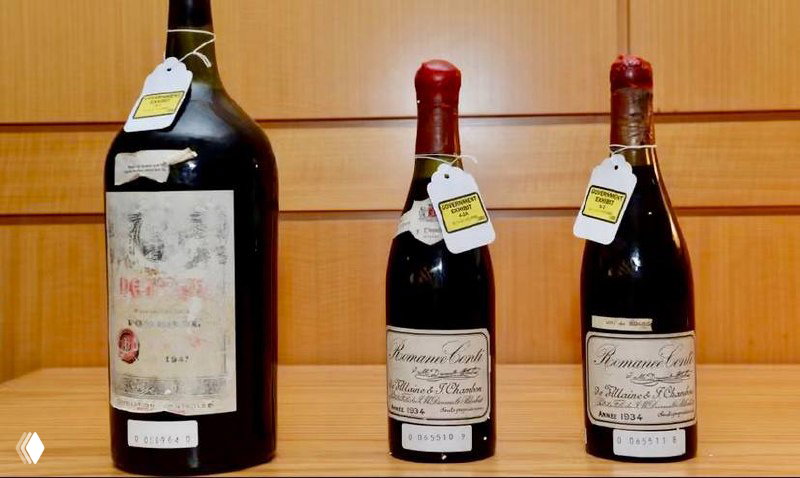 Три бутылки коллекционных вин на столе с бироками и заметными этикетками — кадр из материалов расследования подделок.