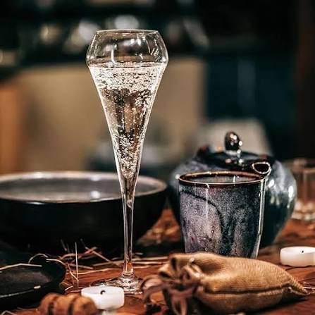 Хрустальный флейт-бокал с игристыми пузырьками на столе рядом с чашкой и предметами сервировки в уютной атмосферe.