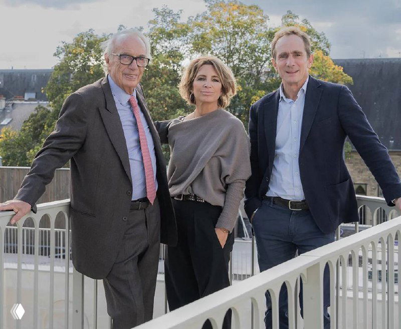 Три человека на террасе у перил — фотография команды или представителей Thiénot на фоне городской застройки и зелёных деревьев в Реймсе.