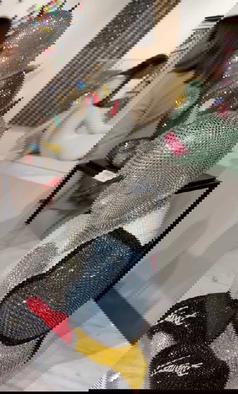 Бюст, покрытый серебристыми стразами с цветными шипами, стоит на столе в галерее; вокруг видны другие объекты и посетители выставки.