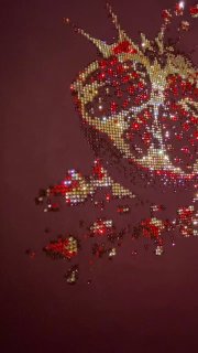 Вертикальный кадр декоративного граната из страз на темно-фиолетовой ткани; мерцающие кристаллы и фрагменты композиции видны сбоку.
