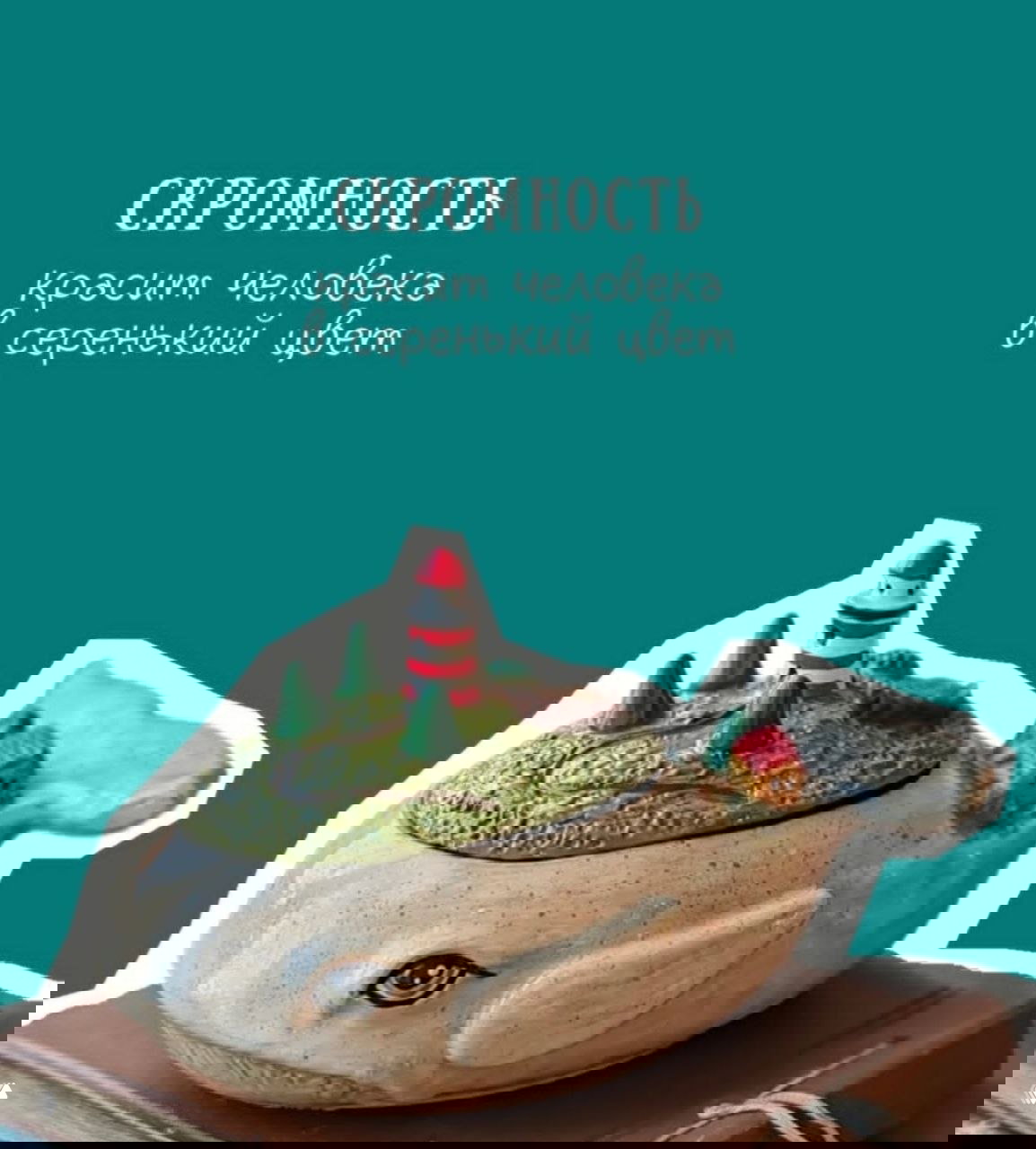 Бирюзовая мотивационная карточка с надписью про скромность и керамической фигуркой кита с мини-маяком и домиком на спине — арт-объект на столе.