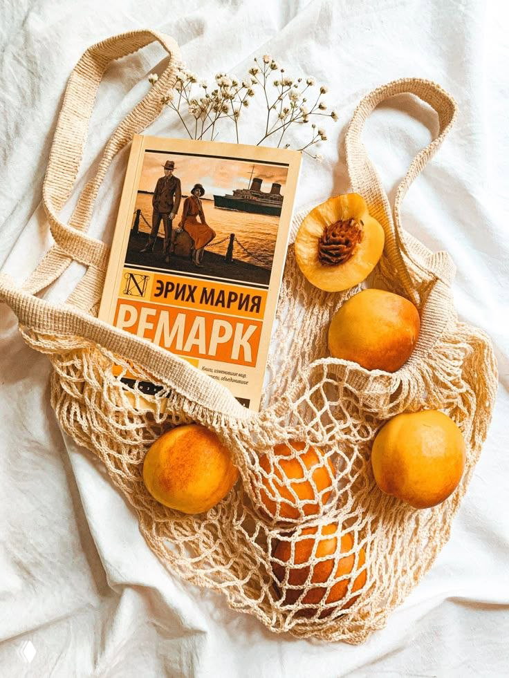 Книга Эриха Марии Ремарка в эко‑сумке рядом с абрикосами на светлом текстиле — тёплый эстетичный кадр для вдохновения.