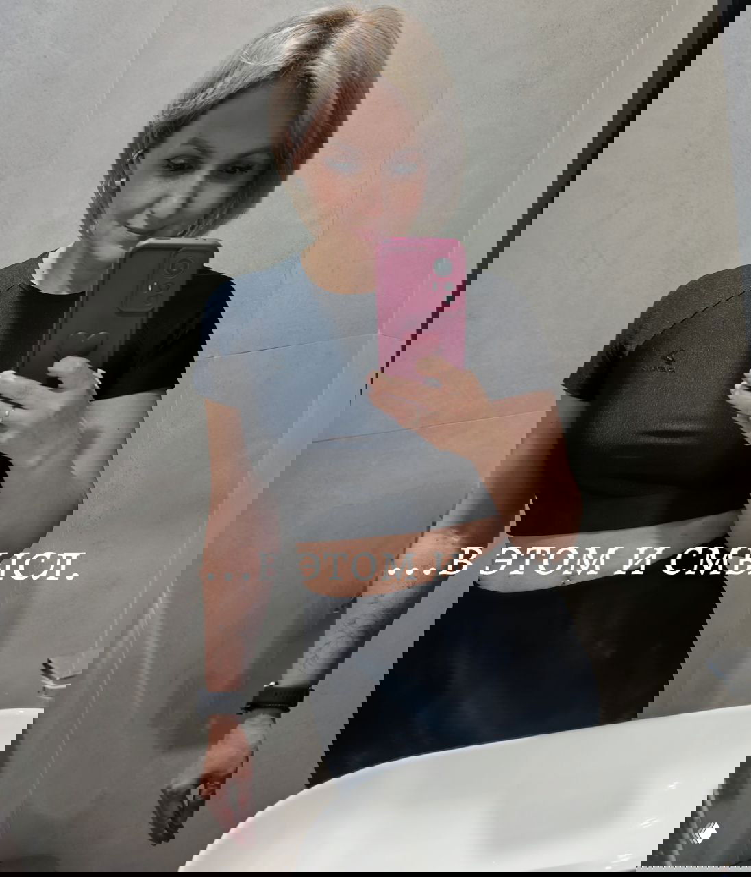 Селфи женщины в спортивном топе перед зеркалом в ванной/раздевалке, видна часть корпуса и рука с телефоном; на фото текст «...В ЭТОМ И СМЫСЛ.», акцент на тренировке и эмоциональном выплеске.