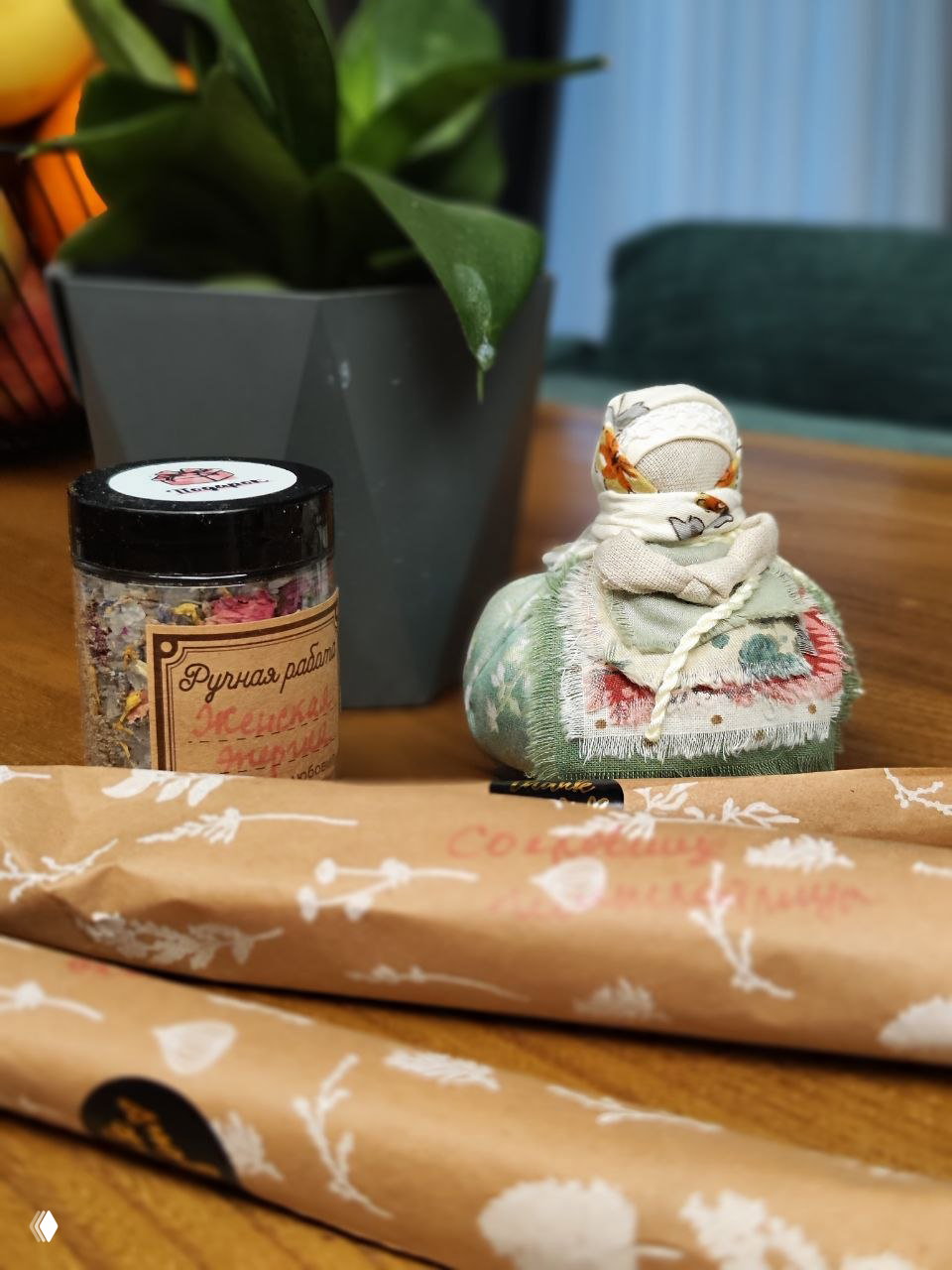Маленькая обережная кукла рядом с баночкой «Ручная работа» и свёрнутой крафт-бумагой — вид композиции на столе после распаковки.