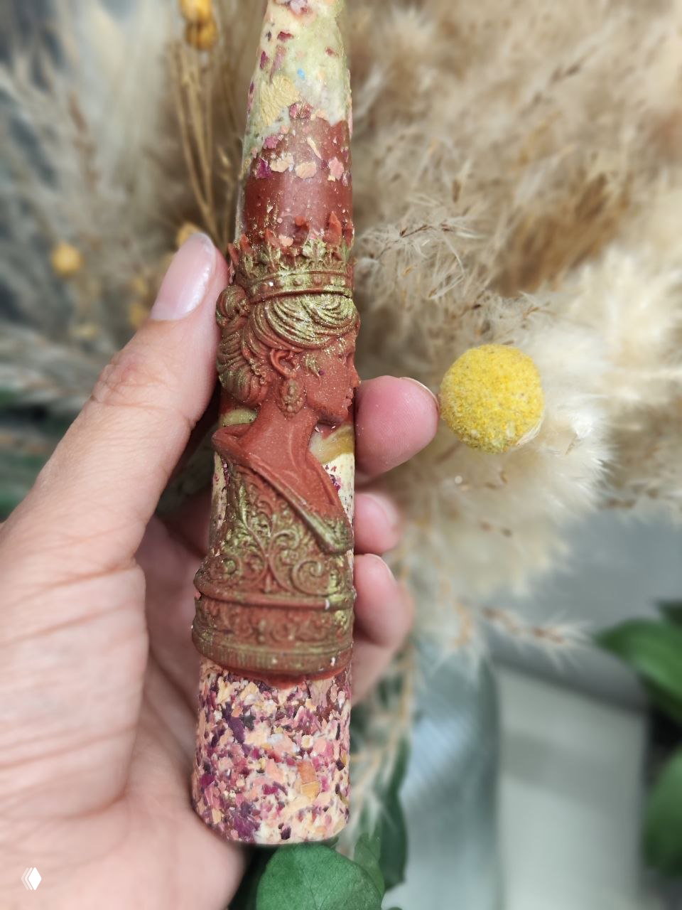 Крупный план декоративной свечи с барельефом в виде короны, текстурой и цветными вкраплениями — рука держит свечу, видны детали отделки.