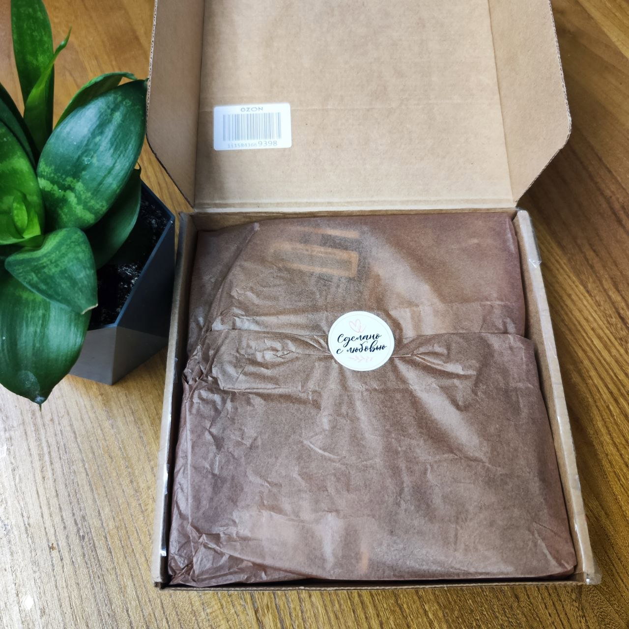 Открытая посылка: коричневая упаковочная бумага с наклейкой «Сделано с любовью» внутри картонной коробки — фотография упаковки перед распаковкой.
