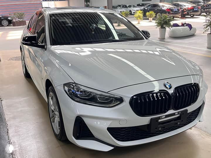 Белый BMW 1 Series 120i M Sport, фокус на передней части и правом крыле; авто стоит в светлом автоцентре с отражениями на капоте.