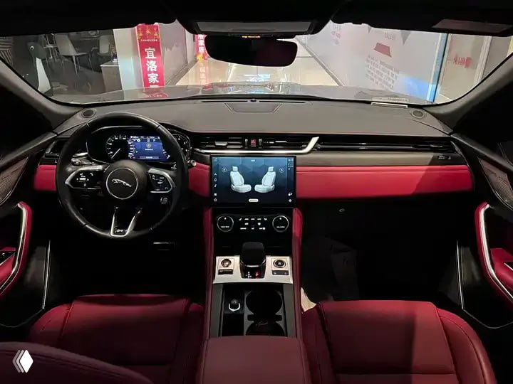 Интерьер Jaguar F‑PACE 2023: торпедо с мультимедиа-экраном, руль и красные кожаные сиденья, крупный план центральной консоли салона.