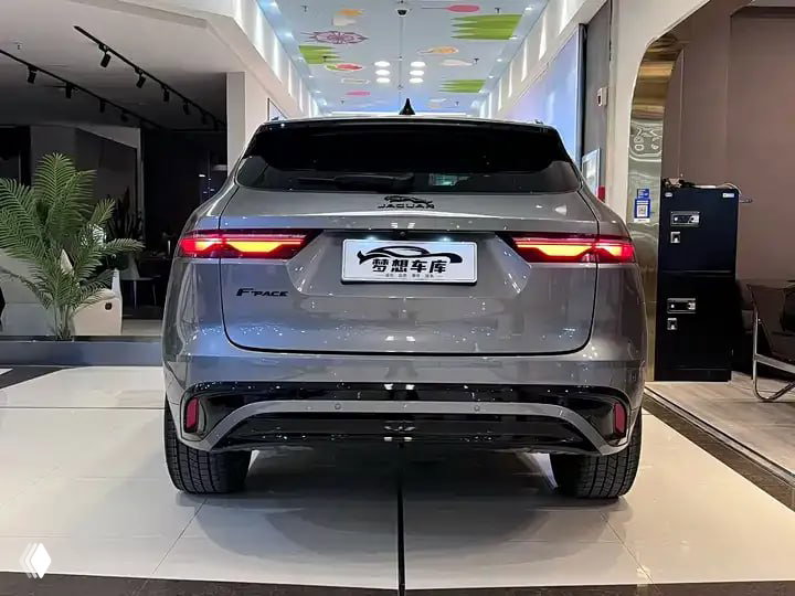 Задний вид Jaguar F‑PACE 2023 в шоуруме: светящиеся фонари, багажник и задний бампер, автомобиль показан на белой напольной поверхности.