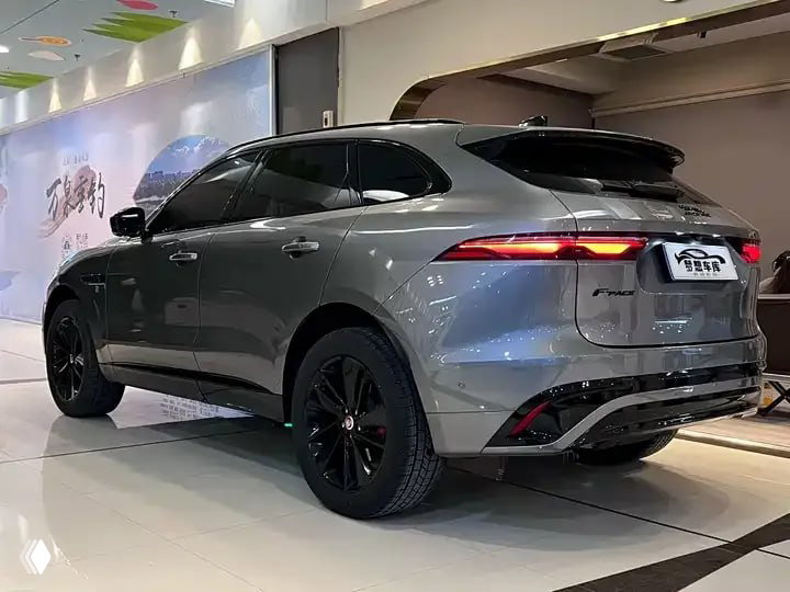 Боковой ракурс Jaguar F‑PACE 2023, вид сзади-справа: серый кузов, чёрные диски и спортивный профиль автомобиля в салоне выставки.