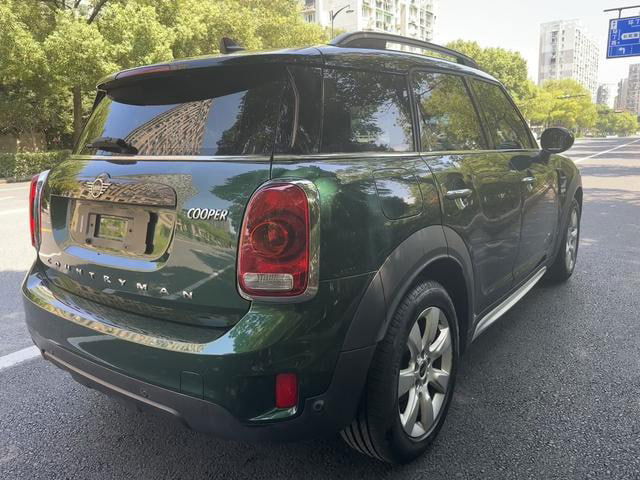 MINI Countryman 2019, вид сзади слева на городском шоссе, кузов с отражениями зданий, чёрная крыша, зелёный корпус