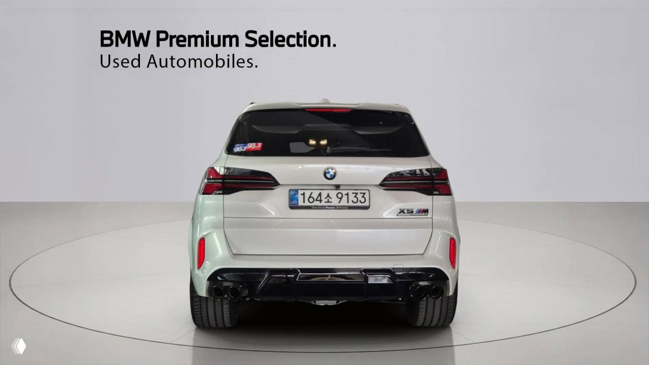 Задняя часть белого BMW X5 M Competition 2025 с видимой корейской номерной табличкой; акцент на диффузоре и выхлопной системе в студии.