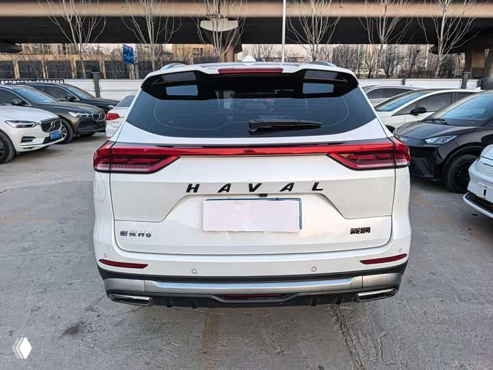 Задняя часть белого Haval H6: крупный план задних фонарей, надпись HAVAL на крышке багажника и вариант бампера в заводской комплектации.