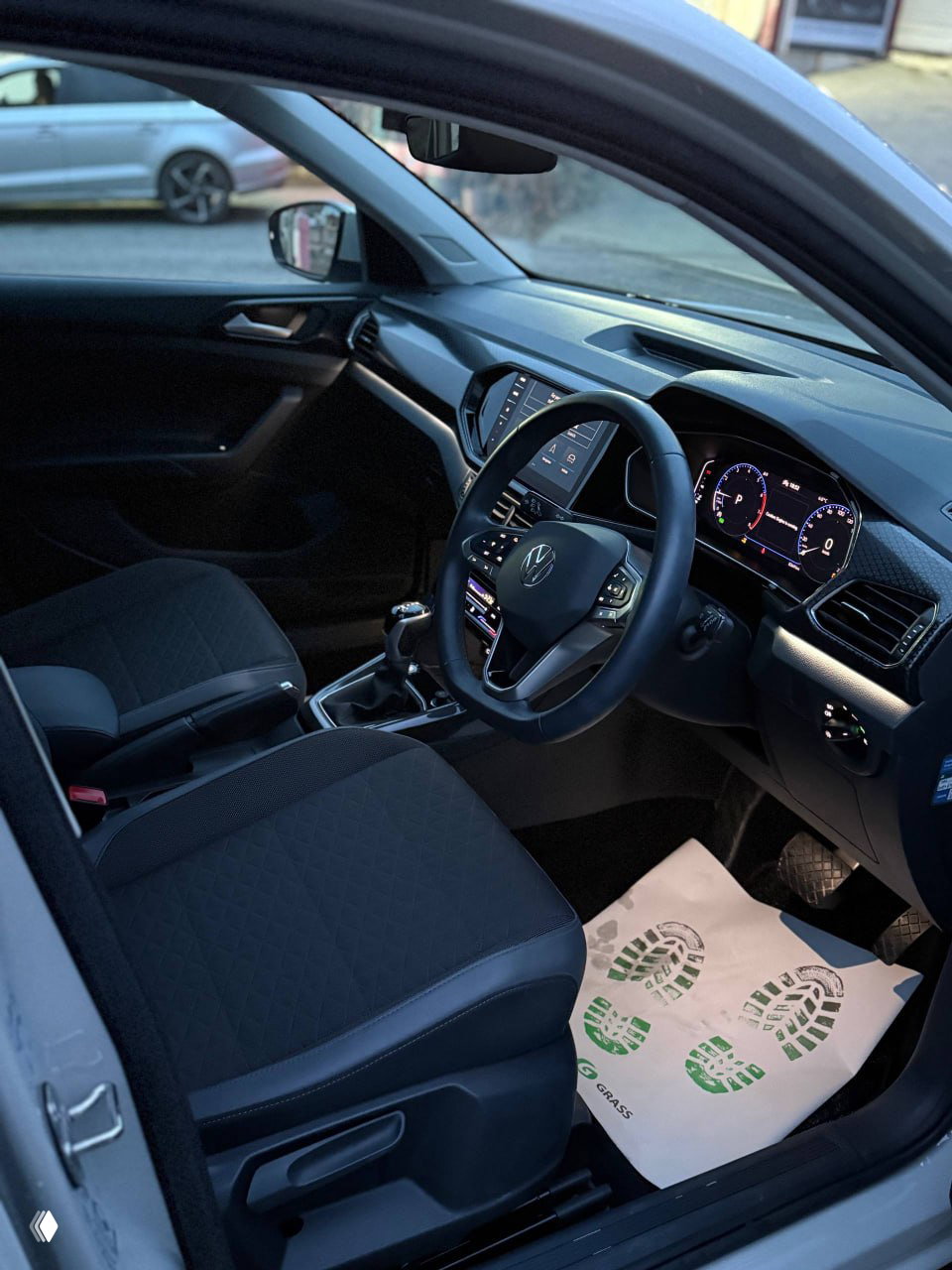 Фронтальная трёхчетвертная съёмка VW T‑Cross с включёнными фарами в сумерках — видна решётка радиатора, передний бампер и колёса в заводском исполнении.