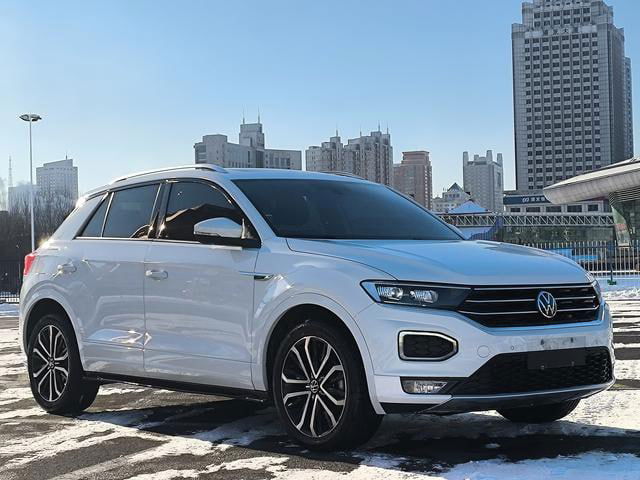 Volkswagen T‑Roc 2021 белого цвета на улице в снежной обстановке, крупный план под углом спереди; демонстрация кузова и дисков колёс.