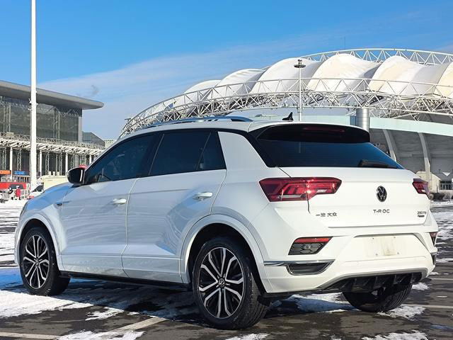 Volkswagen T‑Roc 2021 белого цвета, задний ракурс на парковке рядом с выставочным центром; демонстрация геометрии и лакокрасочного покрытия.