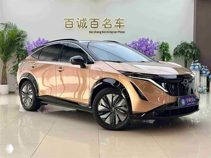 Nissan Ariya в золотистом оттенке, вид спереди-слево в выставочном зале: чёрные акценты, обтекаемый профиль и стильные диски.